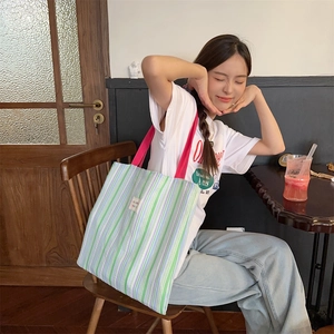 Dettaglio della borsa tote in tela a righe colorate con manici rosa e toppa logo