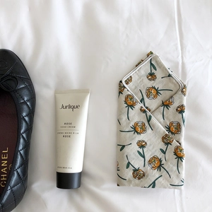 Flat lay of a floral cotton linen scarf next to a black quilted shoe on white bedding