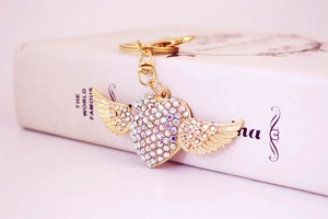 Close-up of golden heart wings keychain with iridescent rhinestones on a book