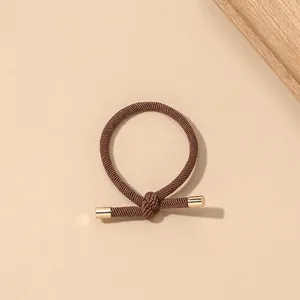Close-up of brown braided elastic hair tie with knotted design and gold metal ends
