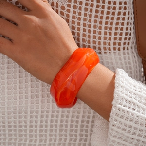 Detailed view of wide orange marbled resin bangle worn on wrist for a stylish fashion look