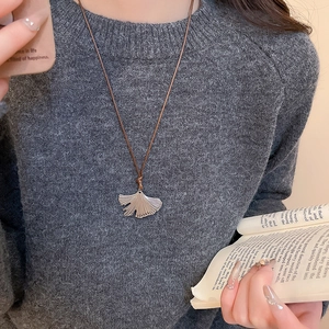 Macro view of silver ginkgo leaf pendant on brown cord worn over a dark grey sweater