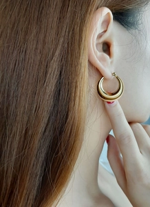 Close-up of a model wearing chunky gold hollow crescent hoop earrings in stainless steel