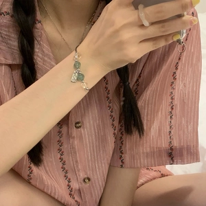Detalle de pulsera de cuentas verdes y claras con colgante de plata grabado en la muñeca
