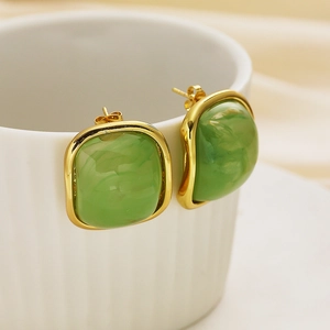 Detailed view of square light green resin earrings with gold edges on a ceramic cup