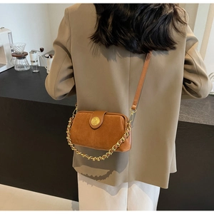 Close-up of caramel suede crossbody bag with vintage gold emblem and metal chain strap