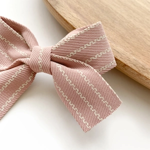 Pink striped fabric bow hair clip for children on a white background with wooden tray