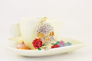 Macro detail of golden skull keychain with red rose and sparkling white rhinestones