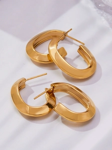 Detailed top view of polished thick gold U-shaped earrings on soft white fabric background