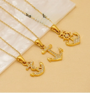Detail of gold nautical anchor pendants with inlaid zircons on a white textured tray
