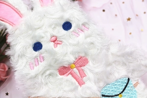 Gros plan sur la trousse lapin en peluche blanche avec broderie fine et texture de fourrure douce