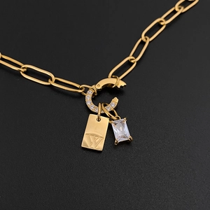 Macro view of gold stainless steel necklace with "W" letter tag and crystal pendant