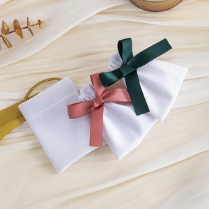 White velvet drawstring jewelry pouches featuring green and pink ribbon bows on fabric