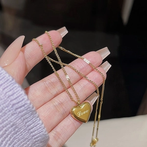 Detail of gold heart pendant necklace with Love engraving and dainty chain held in hand
