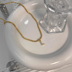 Détail du collier pendentif lettre L dorée avec oxydes de zirconium sur plateau céramique