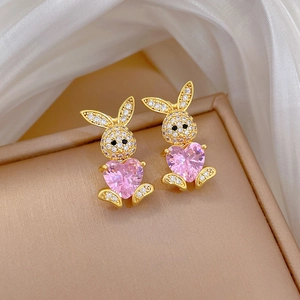 Dettaglio di orecchini a lobo a coniglio dorati con zircone rosa a cuore su scatola beige