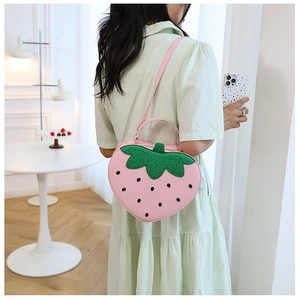 Detail of pink strawberry-shaped shoulder bag with green glitter leaves and long strap