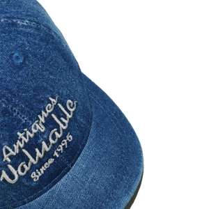 Detailed close-up of white letter embroidery on a washed blue denim short brim baseball cap