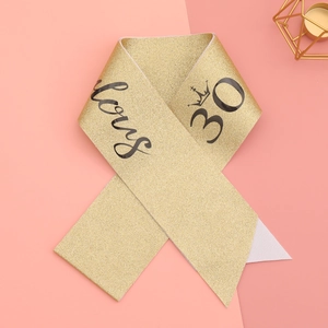 Detail of glittery gold 30th birthday sash featuring crown design and black text