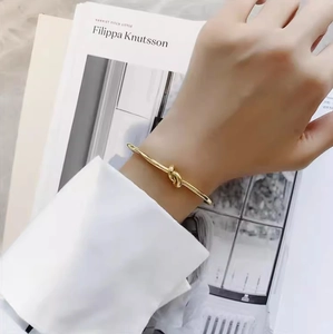 Detailed view of a gold-finish minimalist knotted open bangle on a woman's wrist