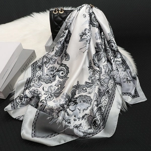 Detail of elegant satin square scarf with vintage floral patterns on a plush white cushion