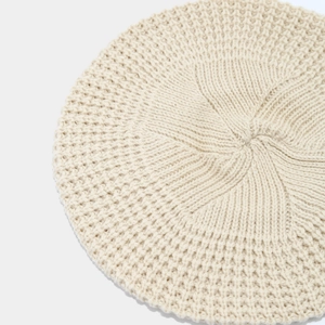 Macro shot of knitted beige beret crown detail showing dense woolen stitching