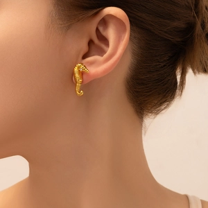 Close-up of a gold-plated seahorse earring with white zircon inlay on model's ear