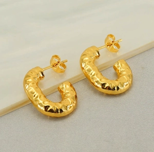 Macro shot of gold-plated C-shaped earrings featuring a vintage hammered metal texture