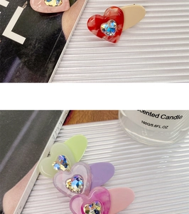 Detail showing candy-colored acetate heart hair clips on white textured background