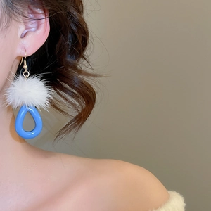 Detail of drop earrings with white plush pompom and blue resin teardrop on model