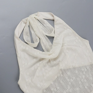 Close-up detail of white lace texture and floral embroidery on backless halter dress