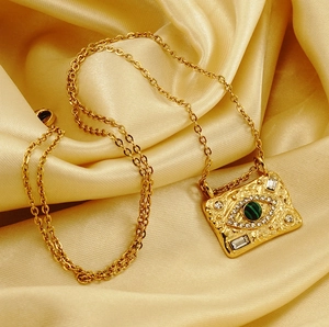Detail of 18K gold necklace with malachite evil eye pendant on golden silk fabric