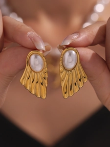 Detailed close-up of shell-shaped gold earrings with white pearl and vintage textures
