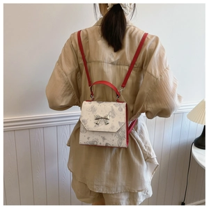 Fashionable white backpack with butterfly prints and red straps shown on a model's back