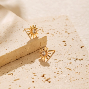 Elegant gold sunflower stud earrings with round cubic zirconia on beige stone surface