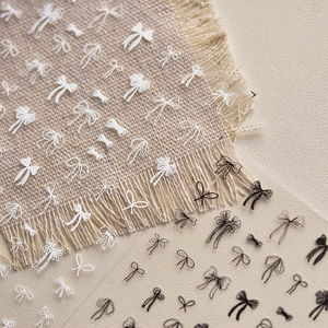 Thin flexible black and white bow nail stickers in hand-drawn style on textured fabric