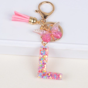 Sequin resin letter L keychain with pink tassel and butterfly charm on white surface
