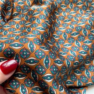 Detail of silk-like orange square scarf featuring blue and green geometric eye pattern