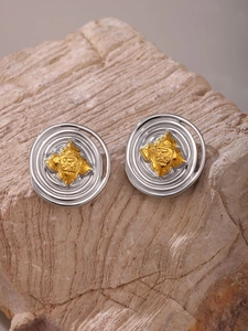 Detail of two-tone stainless steel earrings with gold relief patterns on stone background