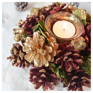 Detail of Christmas candle holder with red pine cones, gold baubles, and lit candle