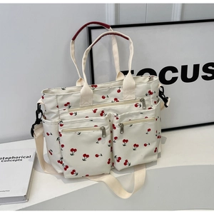 Detail of white canvas tote bag with red cherry print featuring multiple zipper pockets