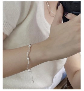 Detail of a wavy silver bracelet with fresh water pearls on a white sweater background