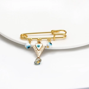 Detail of gold evil eye safety pin brooch with charms on a white porcelain dish