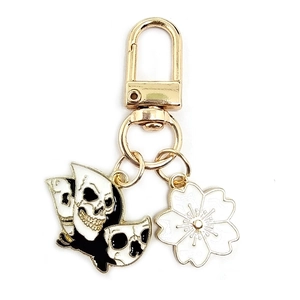 Detail of gold keychain with black and white skull charm and white sakura flower pendant