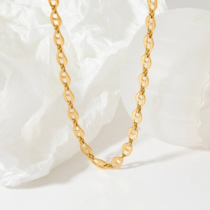 Detail view of a gold pig nose chain necklace on white props with soft lighting shadows