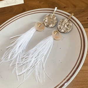 Détail des boucles d'oreilles bohèmes avec plumes blanches, pompons et disques dorés martelés