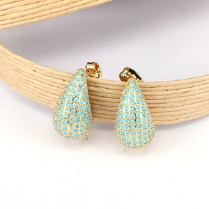 Boucles d'oreilles gouttes dorées avec pierres bleu ciel sur un fond de paille naturelle