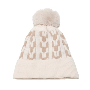 Detail of winter knit beanie with thick cream and coffee geometric patterns and soft pompom