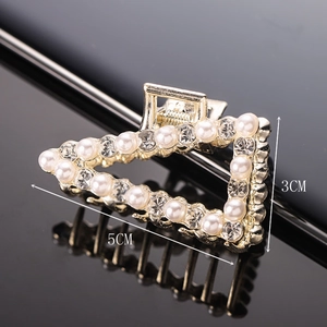 Detailed view of a gold triangle hair claw with white pearls and sparkling rhinestones