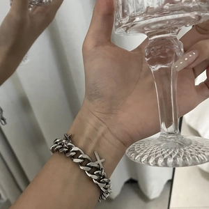 Silver cross pendant Cuban chain bracelet shown on wrist holding a textured glass cup